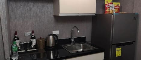 A kitchen with a black countertop, stainless steel sink, and a refrigerator.