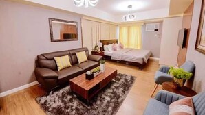 A modern living room with a brown leather sofa, a wooden coffee table, and a grey armchair. - Davao Central Suites (Davao)