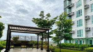 A covered outdoor area with a wooden deck and benches, surrounded by greenery and a modern building with air conditioning units. - Davao Central Suites (Davao)