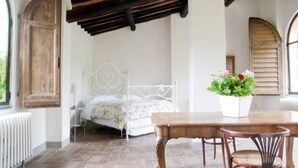 A bedroom with a bed, a wooden table, and chairs. - Flower house, surrounded by greenery, overlooking a large garden. (Bacchereto)