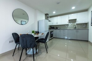A modern kitchen with white cabinets, a refrigerator, and a dining area with a table and chairs. - West Mount Flats (Leeds)