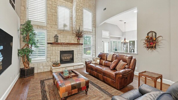 A spacious living room with a stone fireplace, leather sofa, and a large window with shutters.