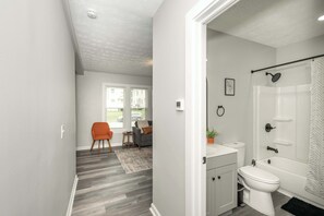 Et moderne badeværelse med toilet, vask og badekar. Der er et bruseforhæng og en potteplante på vasken.