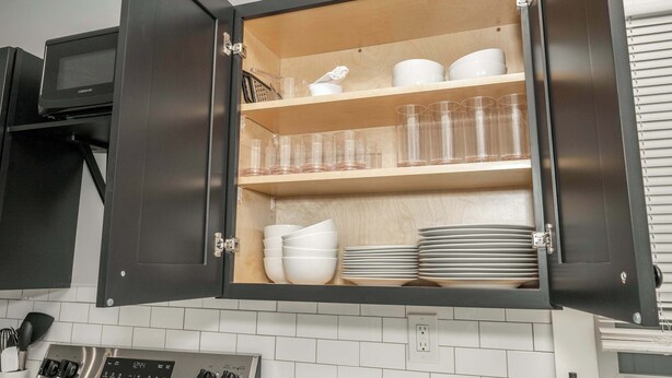 A kitchen with a built-in cabinet containing white bowls, plates, and clear glasses. - Modern Cincy Home – For 6 (Cincinnati)