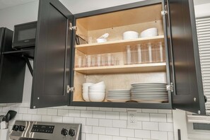 A kitchen with a built-in cabinet containing white bowls, plates, and clear glasses. - Modern Cincy Home – For 6 (Cincinnati)