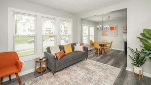 A modern living room with a grey sofa, orange armchair, and a dining area with yellow chairs. - Modern Cincy Home – For 6 (Cincinnati)