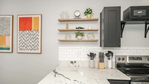 A modern kitchen with white marble countertops, wooden shelves, and stainless steel appliances. - Modern Cincy Home – For 6 (Cincinnati)