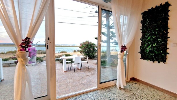 Une pièce dotée d’une porte-fenêtre coulissante donnant sur une terrasse extérieure avec une table et des chaises, une vue sur la mer et un panneau décoratif mural.