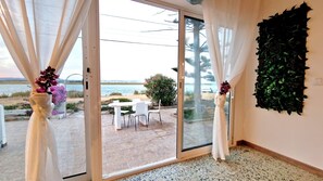 A room with a sliding glass door leading to an outdoor patio with a table and chairs, a view of the sea, and a decorative wall panel. - Do you dream of waking up to the soothing sound of the waves,,,? (Faro)