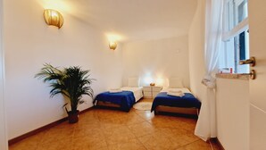 Une chambre d’hôtel avec deux lits, une plante en pot et une fenêtre avec des rideaux.