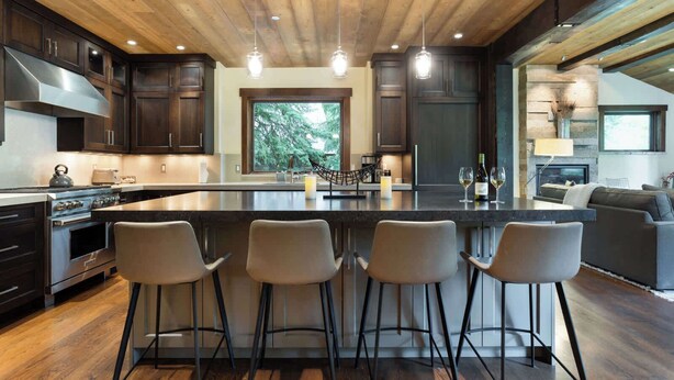 Una cocina moderna con una isla grande, taburetes de bar, armarios de madera oscura, electrodomésticos de acero inoxidable y una chimenea de piedra.