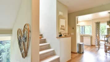 A staircase leading to a second floor with a view of greenery outside. A kitchen area with a sink and cabinets is visible.