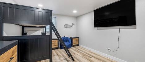 A room with a bunk bed, a TV mounted on the wall, and a window.