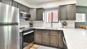 Een moderne keuken met roestvrijstalen apparatuur, donkere houten kastjes, een wit aanrecht en een raam met blinds.