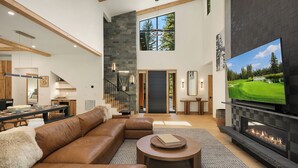 Un amplio salón con un sofá modular grande, una chimenea y un televisor que muestra un campo de golf.