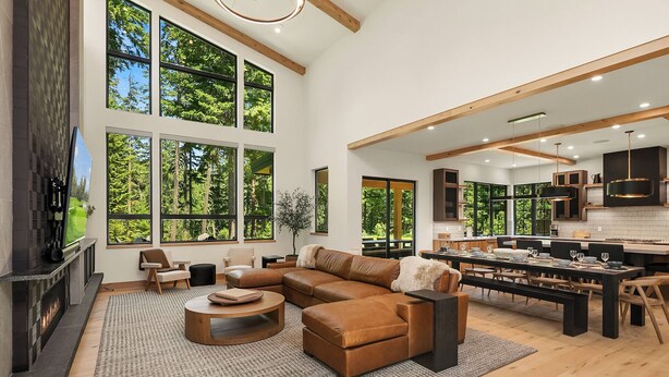 Amplia sala de estar con un sofá seccional grande, una chimenea y ventanas amplias con vistas al bosque.