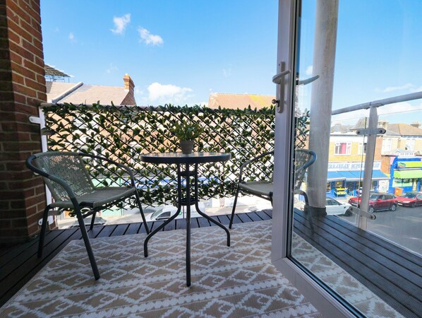 A balcony with two chairs and a table, a patterned rug, and a view of buildings and a street.