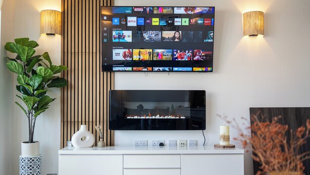Un salon moderne avec un téléviseur à écran plat fixé au mur, un meuble de rangement blanc en dessous et deux lampes murales.