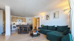Un salon moderne avec un canapé vert, une table basse et une cuisine en arrière-plan.