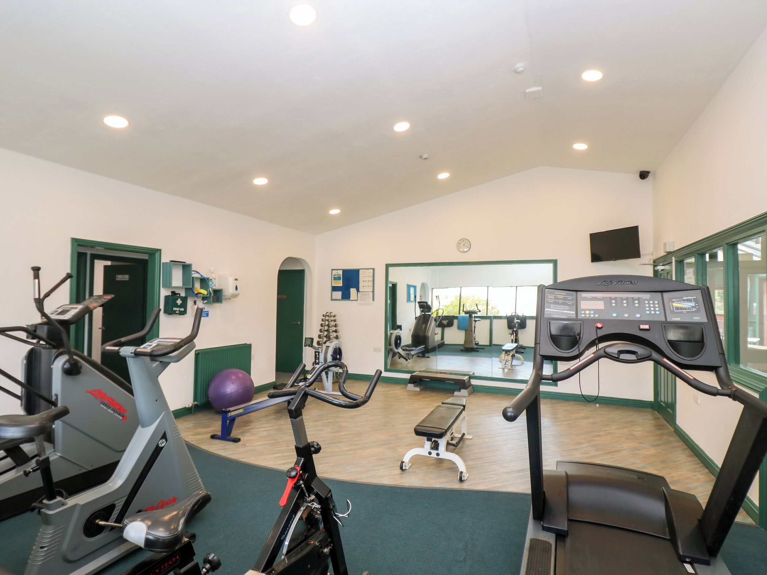 A gym with stationary bikes, a treadmill, and a mirrored wall.