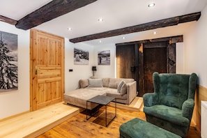 A cozy living room with a wooden floor, a sofa, a green armchair, and a wooden door. - Kaiserberg Apartment with Garden BBQ Hut and Views of the Beautiful Bernau Valley (Bernau im Schwarzwald)
