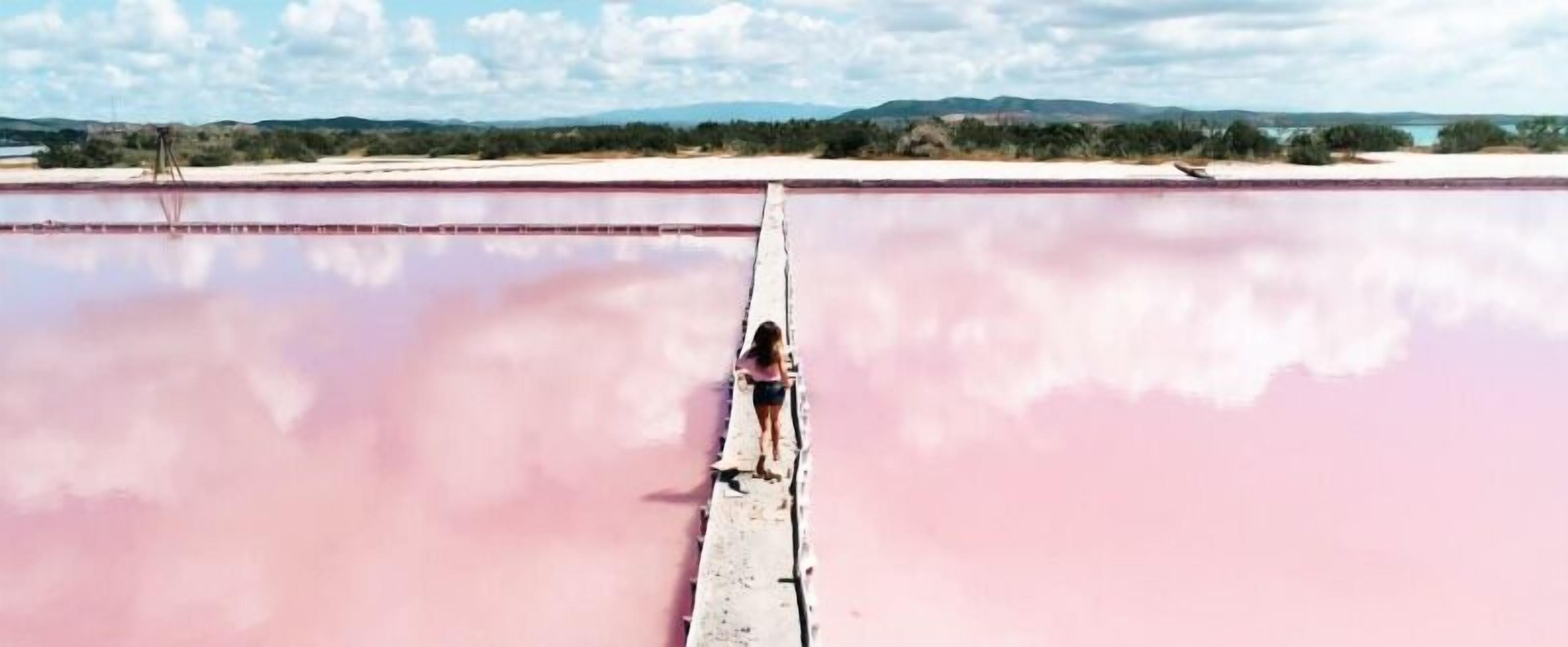 Una persona de pie sobre un puente estrecho sobre una gran extensión de agua, con un paisaje al fondo.