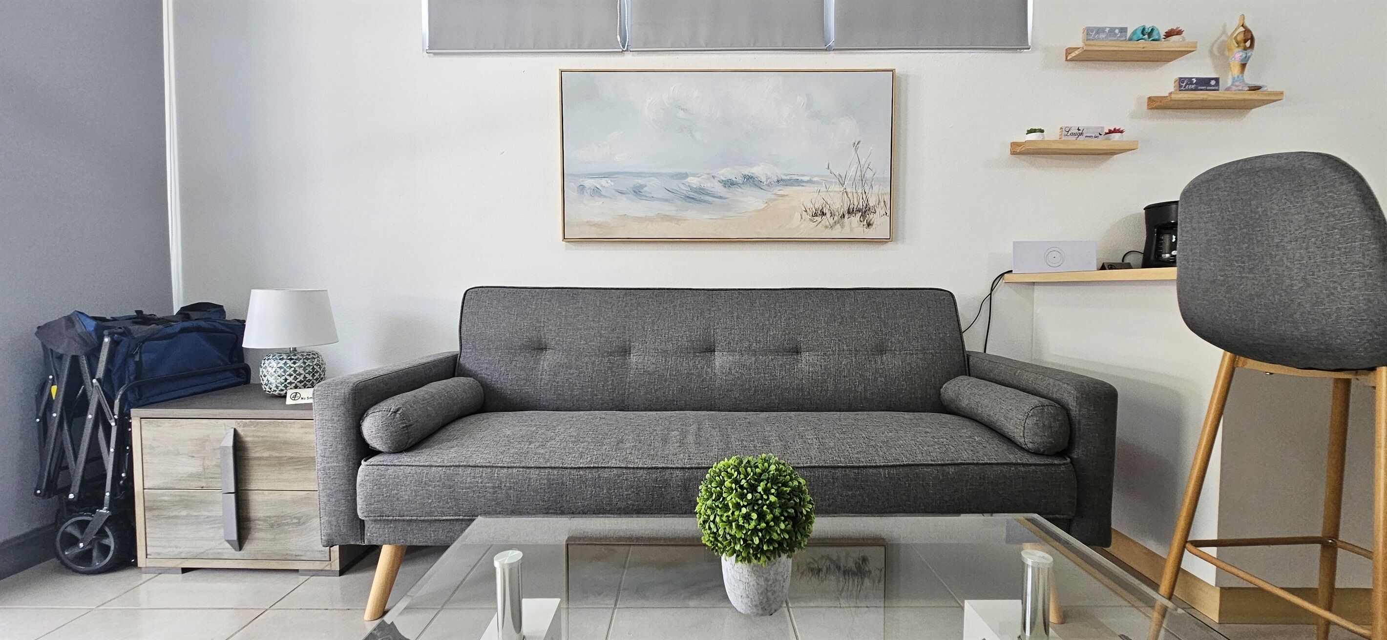 Uma sala de estar moderna com um sofá cinzento, uma mesa de centro com uma planta, uma luminária e um pequeno armário.