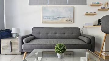 Uma sala de estar moderna com um sofá cinzento, uma mesa de centro com uma planta, uma luminária e um pequeno armário.