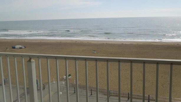 Uitzicht op een strand vanaf een balkon met een hekwerk, zandstrand en zee.