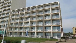 Een hotel met meerdere verdiepingen, balkons, een plat gevelvlak en een parkeerplaats ervoor.