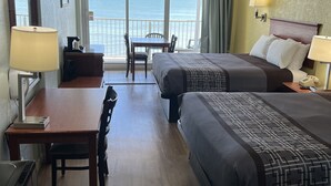Een hotelkamer met twee bedden, een bureau, een stoel, een tafel en een balkon met uitzicht op zee.