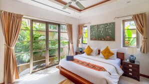 A bedroom with a large bed, a ceiling fan, and a view of greenery through the windows. - Exotic Pool Villa Solandra in Bangtao (Choeng Thale)