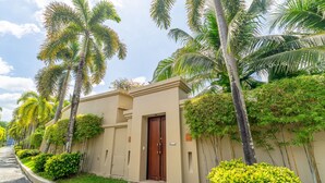 A modern building with a brown door, surrounded by lush greenery and palm trees. - Exotic Pool Villa Solandra in Bangtao (Choeng Thale)