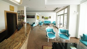 A lobby with a reception desk, teal armchairs, and a large window providing natural light. - Okutur Otel (Rize)