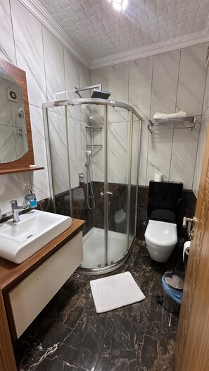 A bathroom with a glass-enclosed shower, a white sink, a toilet, and a mirror. - Okutur Otel (Rize)