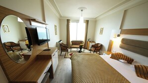 A hotel room with a bed, a desk with a TV, a chair, a sofa, and a mirror. - Okutur Otel (Rize)