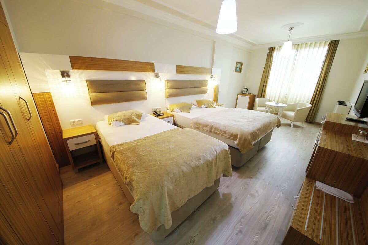 Quarto de hotel com duas camas, uma escrivaninha, uma cadeira, uma televisão e um guarda-roupa.