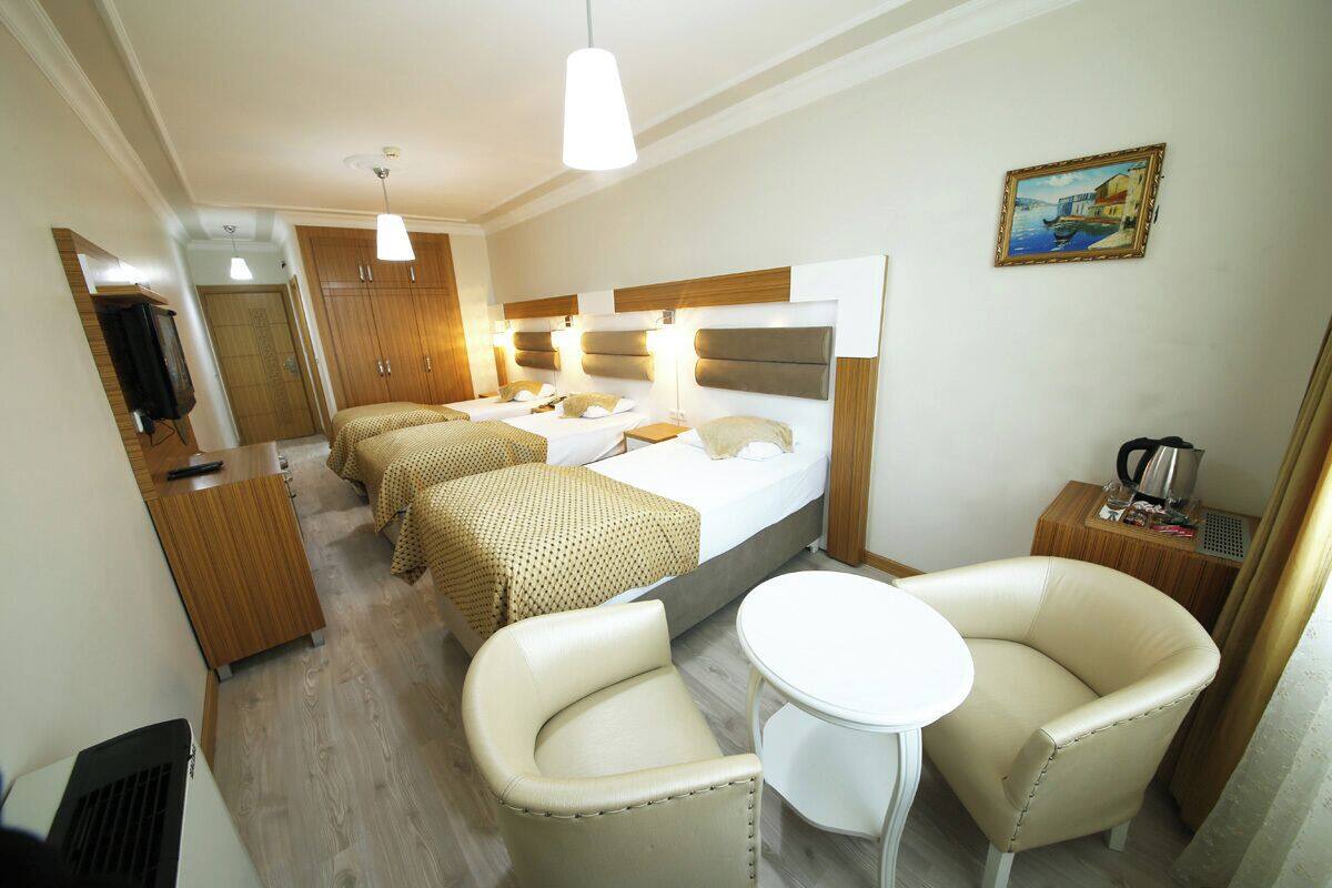 Quarto de hotel com uma cama, duas mesas de cabeceira, uma escrivaninha, uma cadeira, uma mesinha e um quadro na parede.