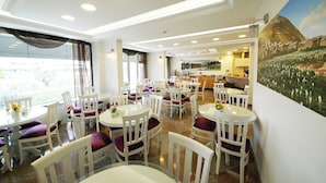 A dining area with round tables and chairs, a kitchen in the background, and a mural on the wall. - Okutur Otel (Rize)
