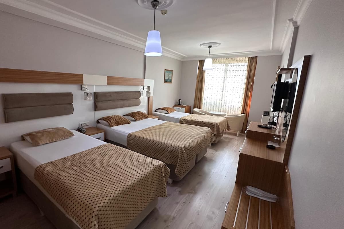 Quarto de hotel com três camas, uma escrivaninha, uma cadeira, uma televisão e uma janela com cortinas.