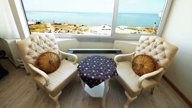 A room with two beige armchairs facing a large window overlooking a beach and ocean. - Okutur Otel (Rize)