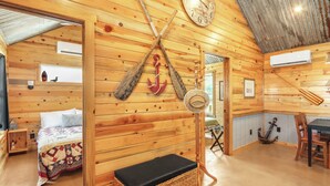 Ein Holzblockhaus-Innenraum mit einem Bett, einem Esstisch und einer an der Wand hängenden Uhr.