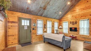 Une cabane confortable avec un intérieur en bois, un lit, une télévision et une fenêtre avec des rideaux.