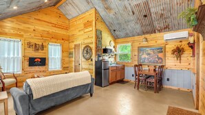 L’intérieur chaleureux d’un chalet en bois comprend un canapé, une table à manger, un coin cuisine et une grande fenêtre.