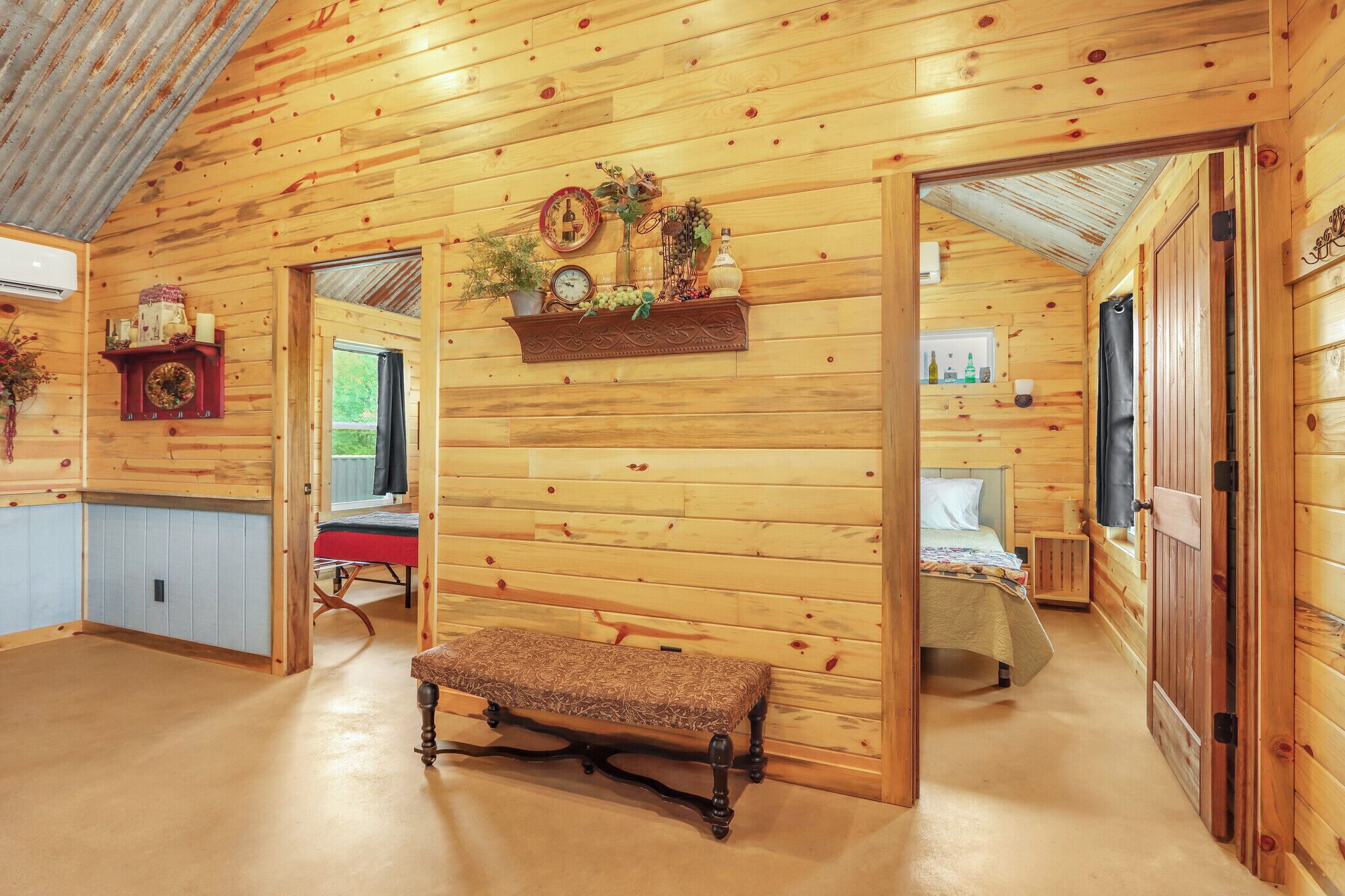 A wooden cabin interior with a bench, a shelf with decorative items, and a bed.