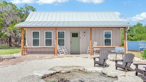 Un petit bâtiment d’un seul étage, doté d’un toit en métal et portant le numéro 5, avec une véranda agrémentée de chaises Adirondack et d’un barbecue.