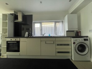 Cucina compatta con forno integrato, lavatrice e finestra con tende leggere.
