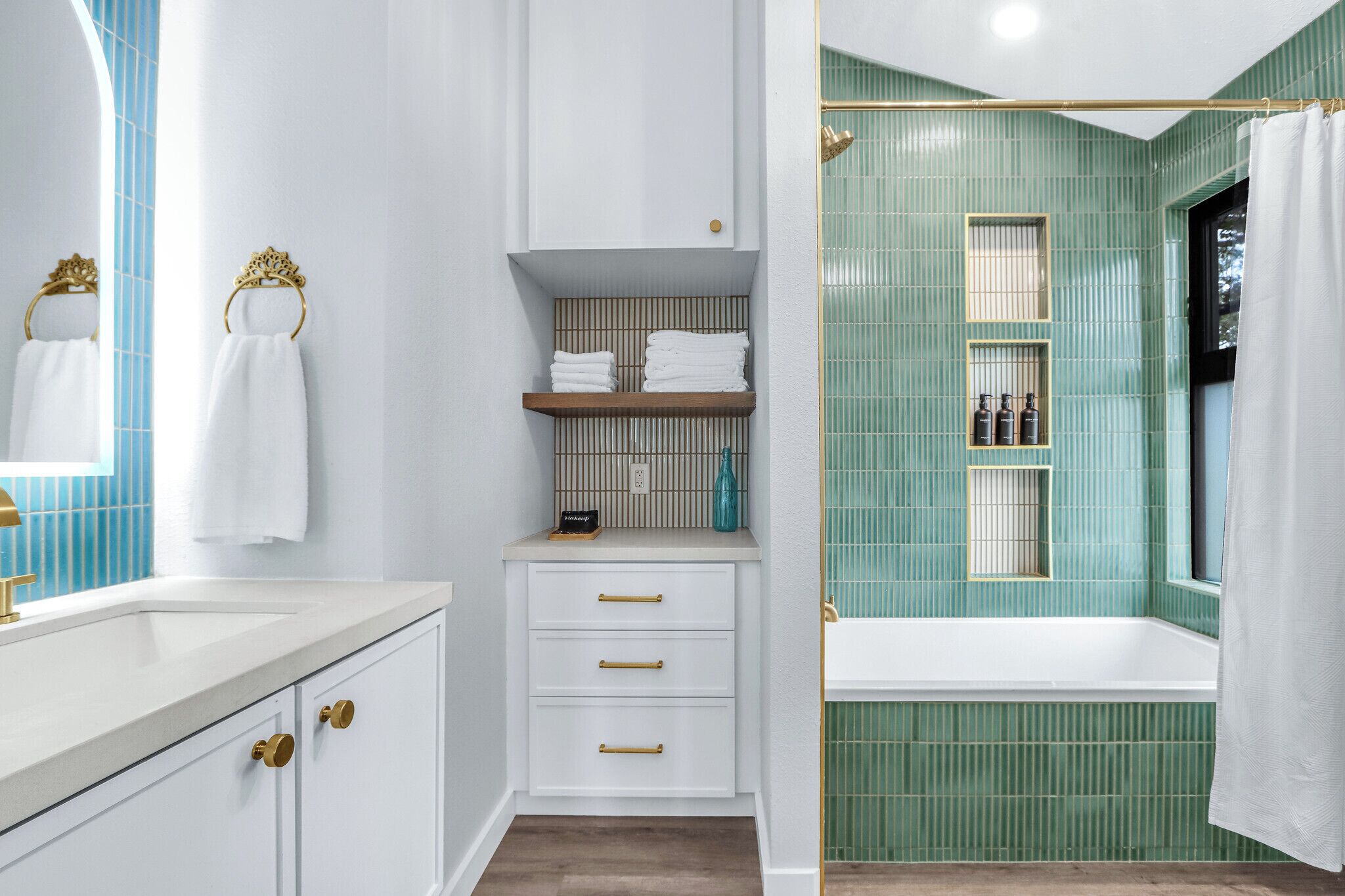 A bathroom with a white vanity, a mirror, and a green-tiled shower area.