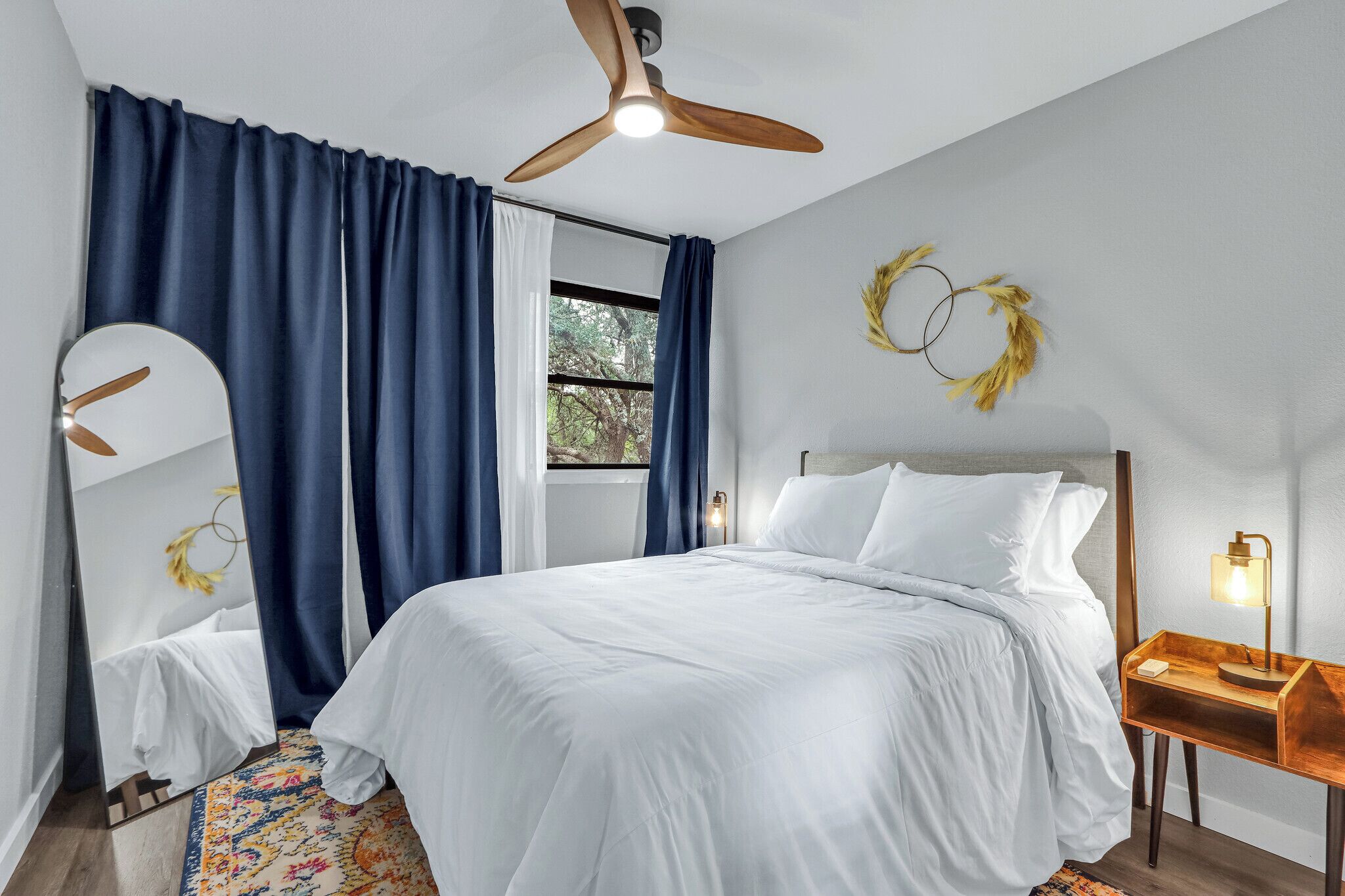 Une chambre à coucher avec un lit, un ventilateur de plafond, une table de chevet avec une lampe et une fenêtre avec des rideaux.