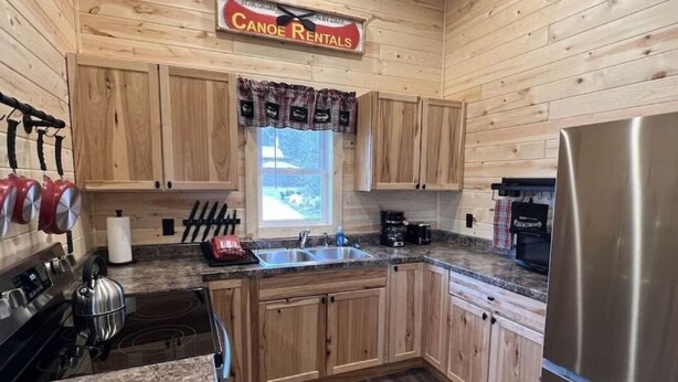 Interior de una cabaña de madera con cocina, que incluye estufa, lavaplatos y refrigerador.